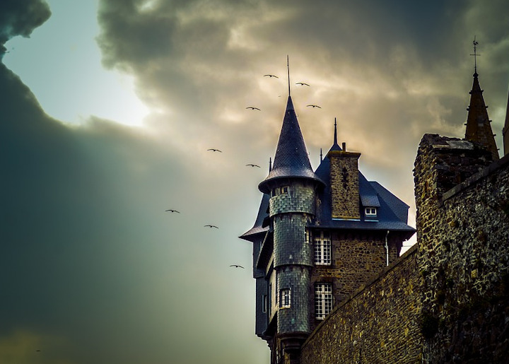 A gothic building turret with birds flying around it